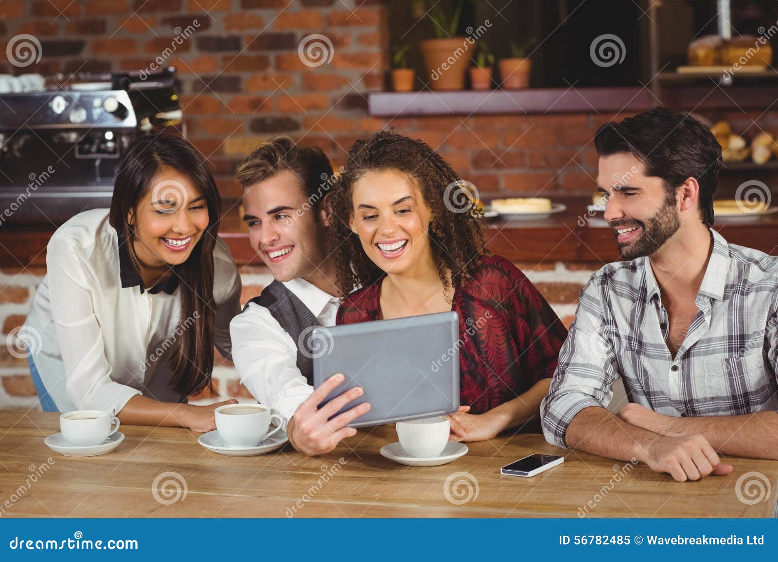 Amigos de sorriso que olham a tabuleta digital na cafetaria