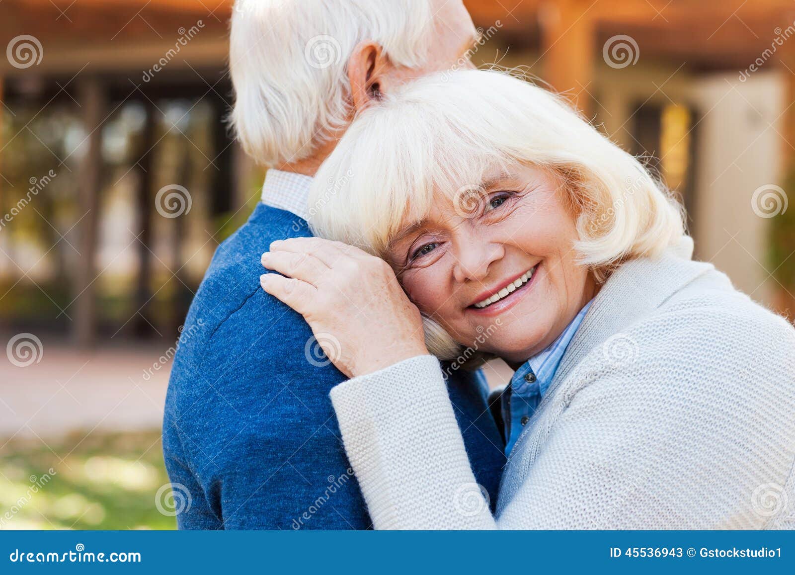 Amour pour toujours. Femmes supérieures heureuses se penchant à l'épaule de son mari et souriant tandis que chacun des deux se tenant dehors et devant leur maison