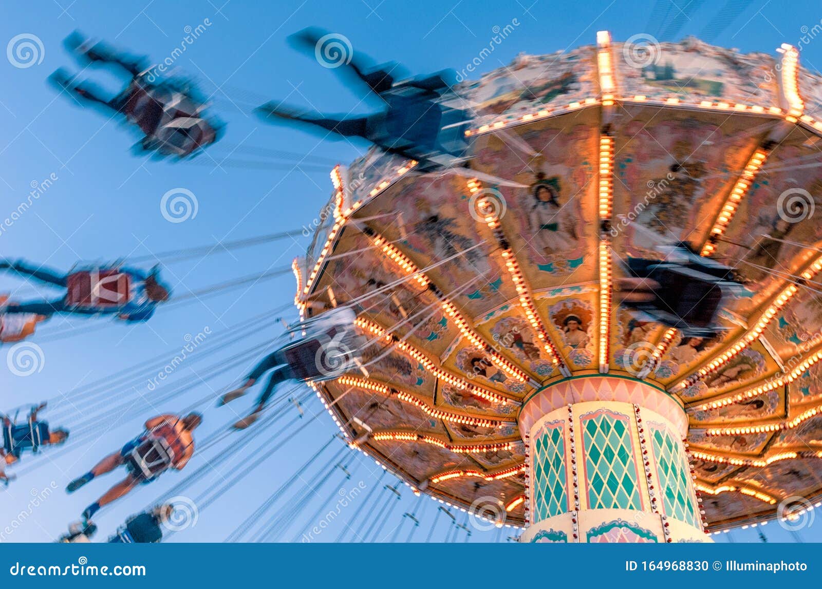 amusement park motion blurred riders on retro vintage tilting swing against clear blue sky.