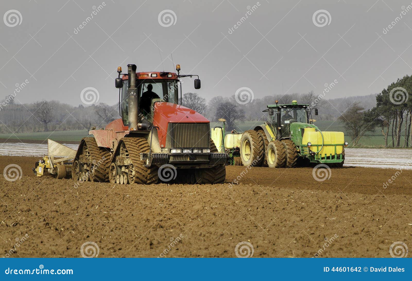 Anbaufläche und bohrender Mais. Traktor mit Bohrgerätsäenmais und -bedeckung es mit dem biologisch abbaubaren Polythen, zum von Keimung zu unterstützen Der Mais wird für Tierfutter oder Brennstoff für Kraftwerke benutzt Auch ein Traktor, der den Boden für das Säen vorbereitet