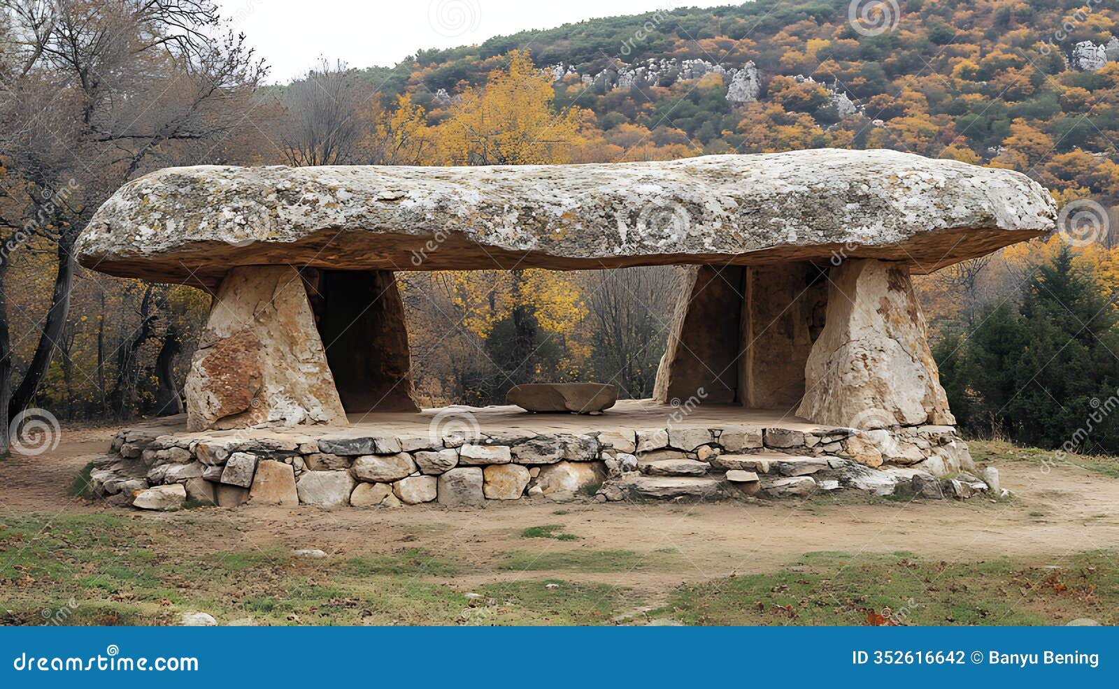 ancient stone structure with a large flat top, supported by two pillars, in a wooded area with fall foliage