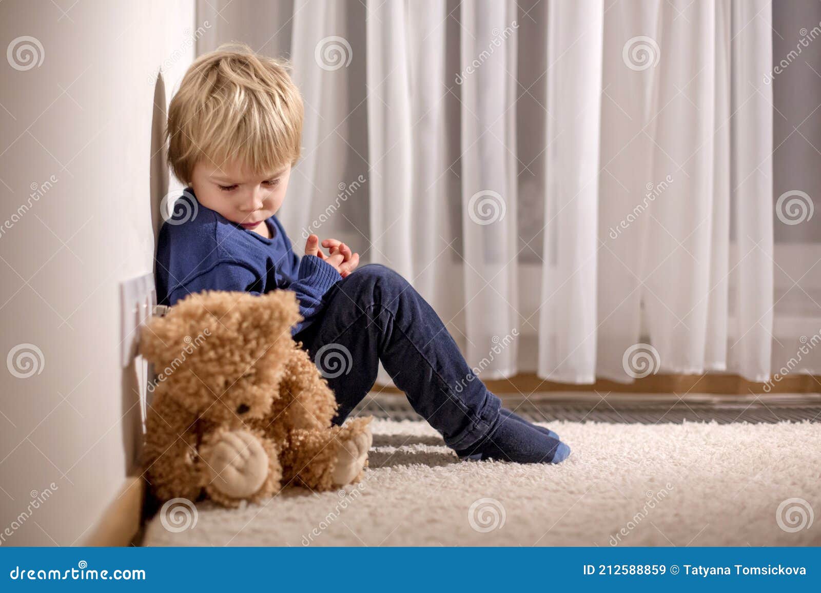 angry little toddler child, blond boy, sitting in corner with teddy punished for mischief