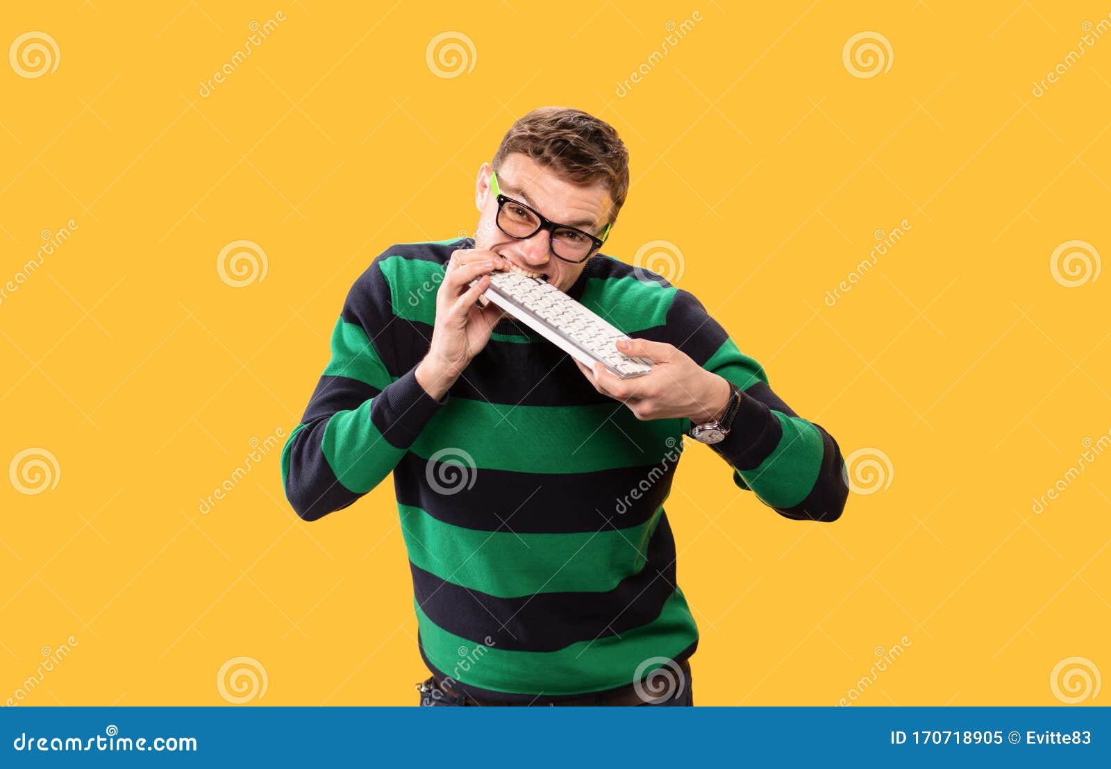 Angry Young Man Holds A Keyboard In His Hands And Bites It On Yellow angry-young-man-holds-a-keyboard-in-his-hands-and-bites-it-on-yellow
