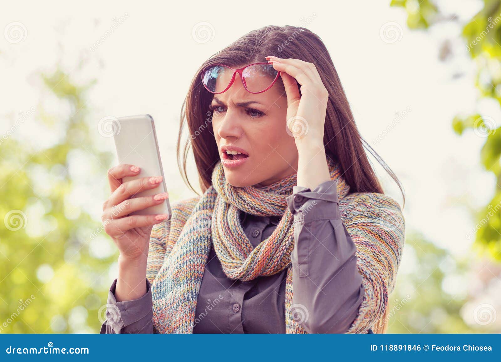 annoyed upset woman in glasses looking at her smart phone with frustration while walking on a street