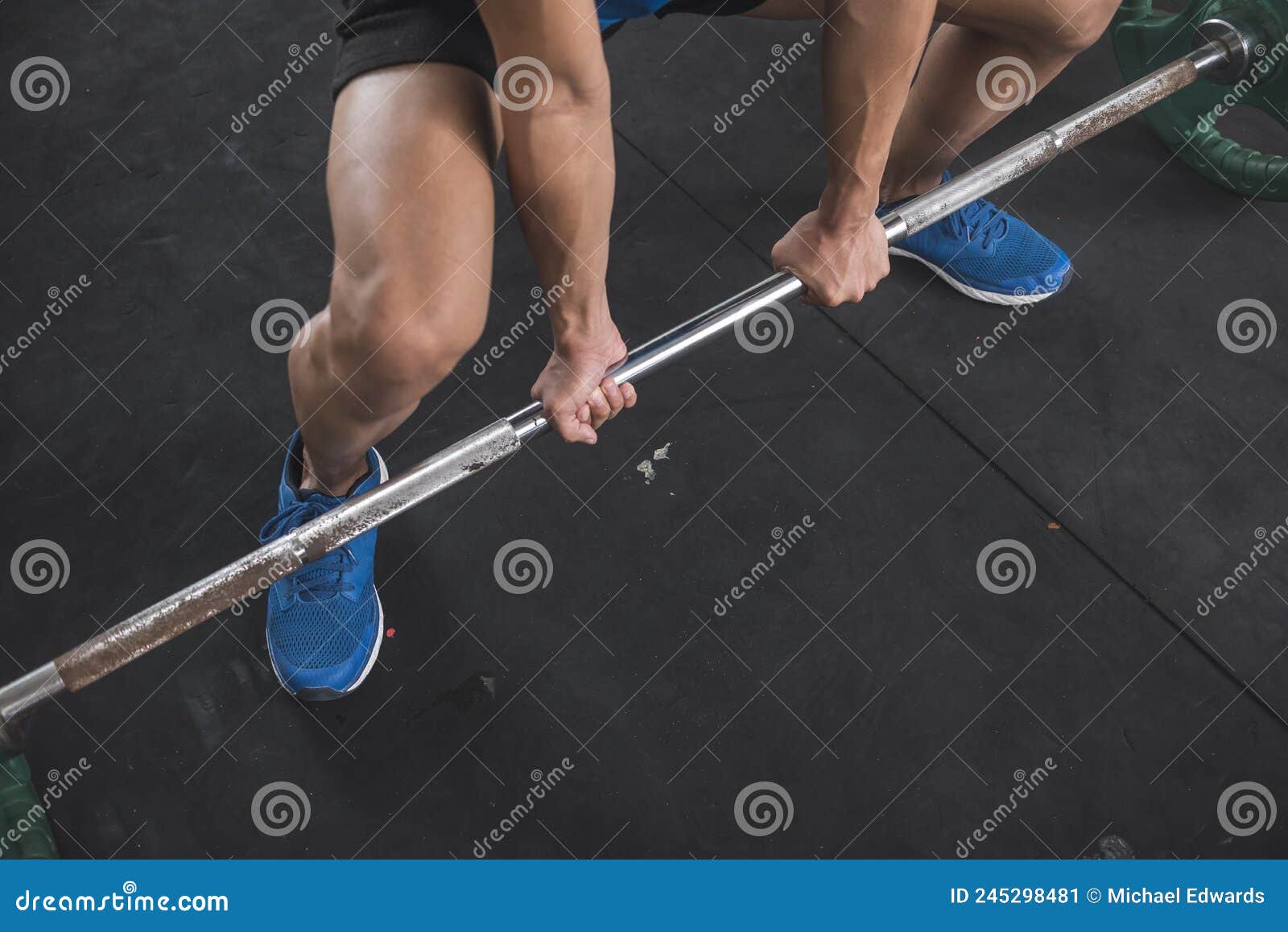 an anonymous man doing sumo deadlifts. using an alternate grip to pick up the barbell. overhand on left hand and underhand on the
