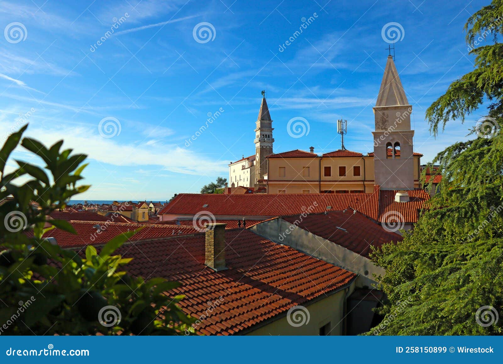 buildings and trees in the city of piran, eslovenia with a church and a blue sky in the background.
