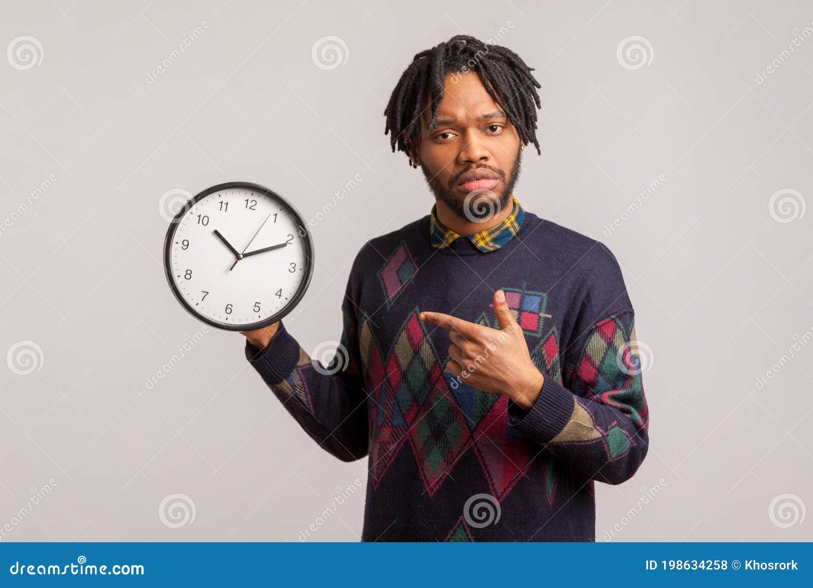 anxious displeased man with dreadlocks and beard pointing finger on wall clock in his hand. i need more time