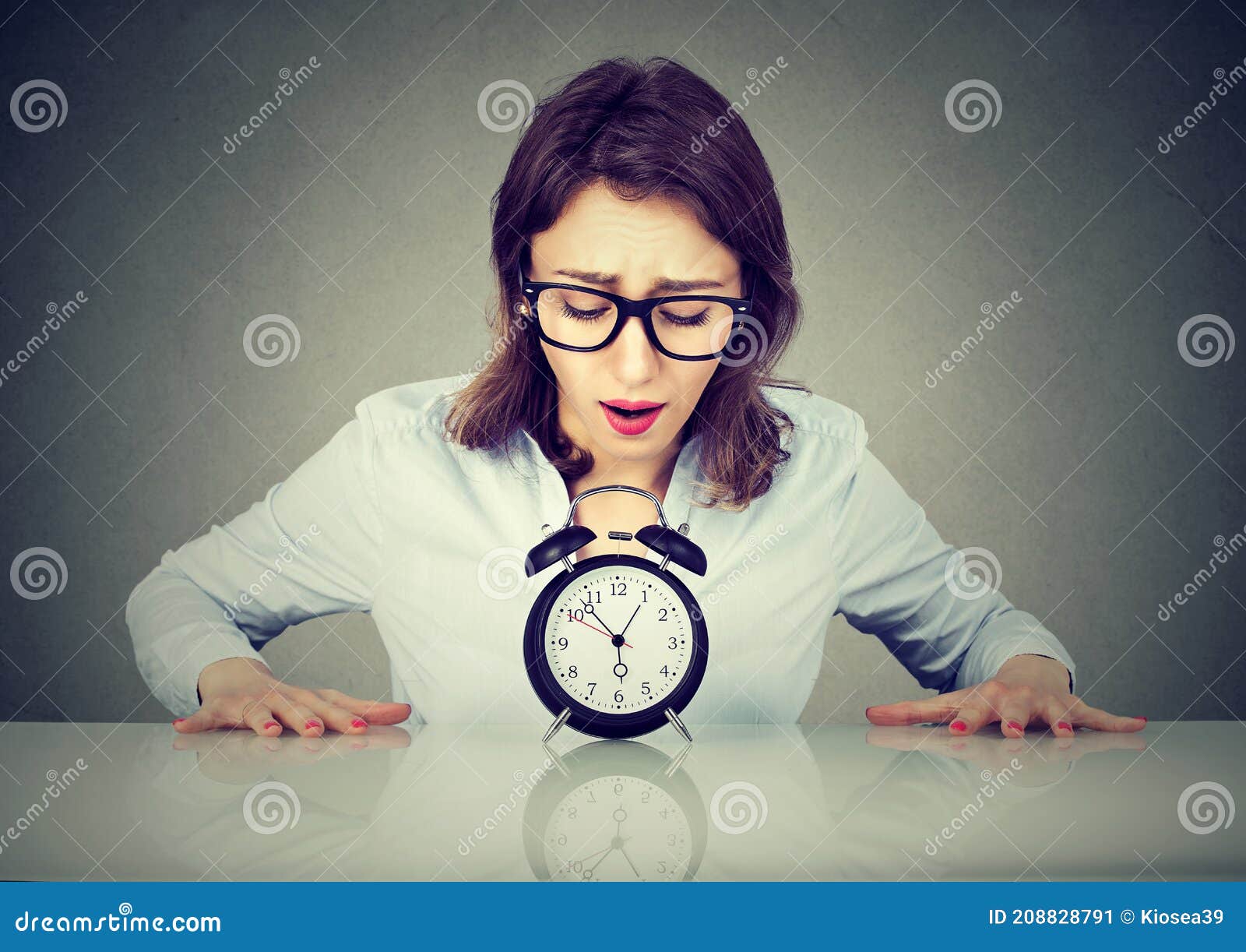 Anxious Woman Sitting at Table Looking at Alarm Clock Stock Image
