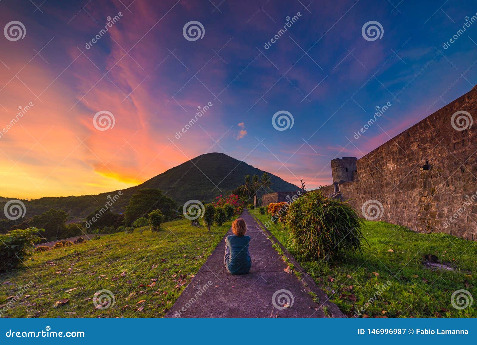 api volcano at sunset, sitting woman looking at view from banda naira fort, maluku moluccas indonesia, top travel tourist