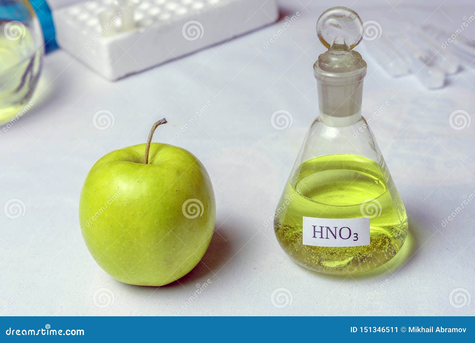 an apple and a chemical flask labeled nitric acid - nitrate. the concept of the presence of nitrates and gmos