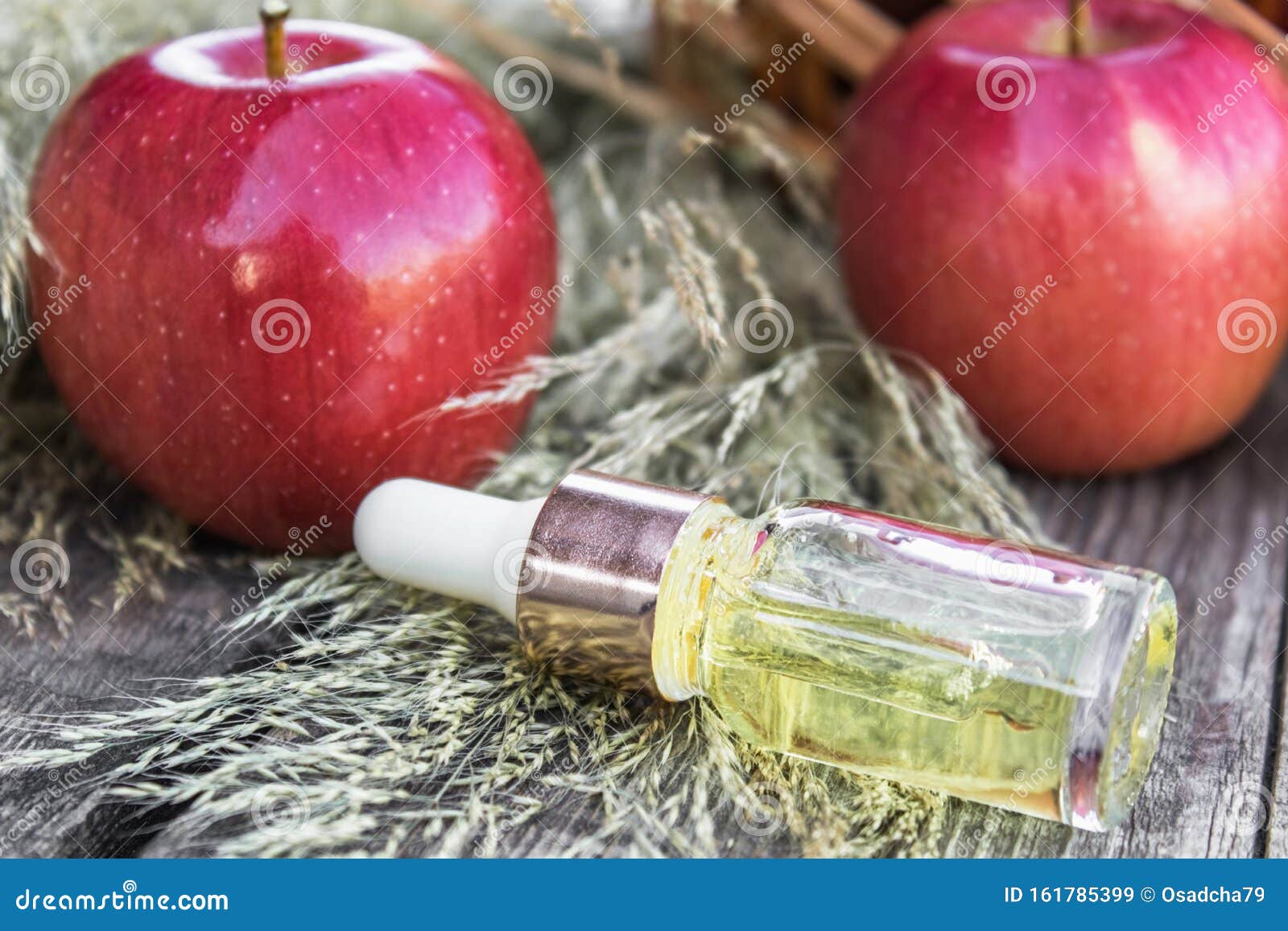 Glass bottle of apple essential oil near fresh apples on a wooden