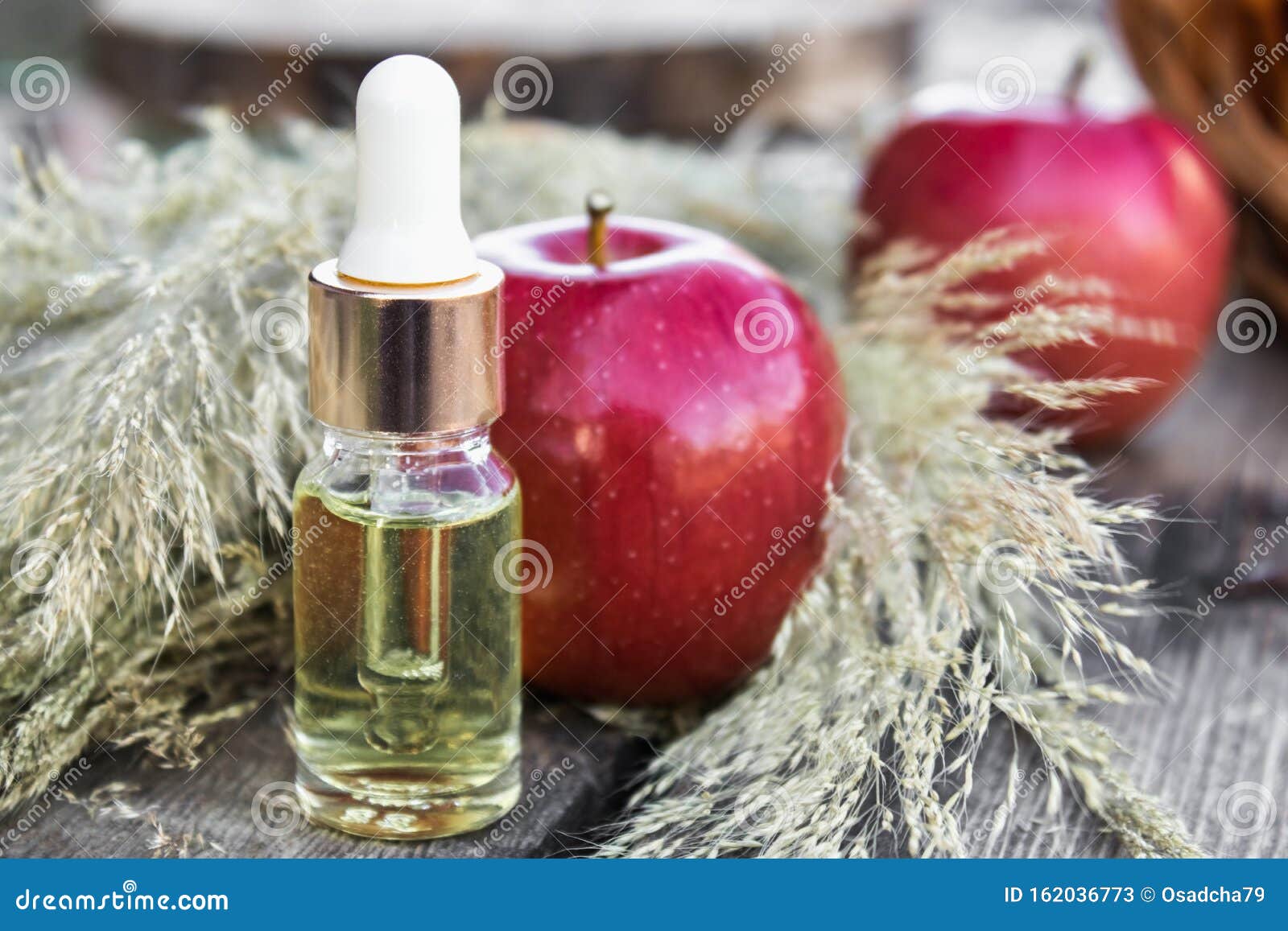 Glass bottle of apple essential oil near fresh apples on a wooden