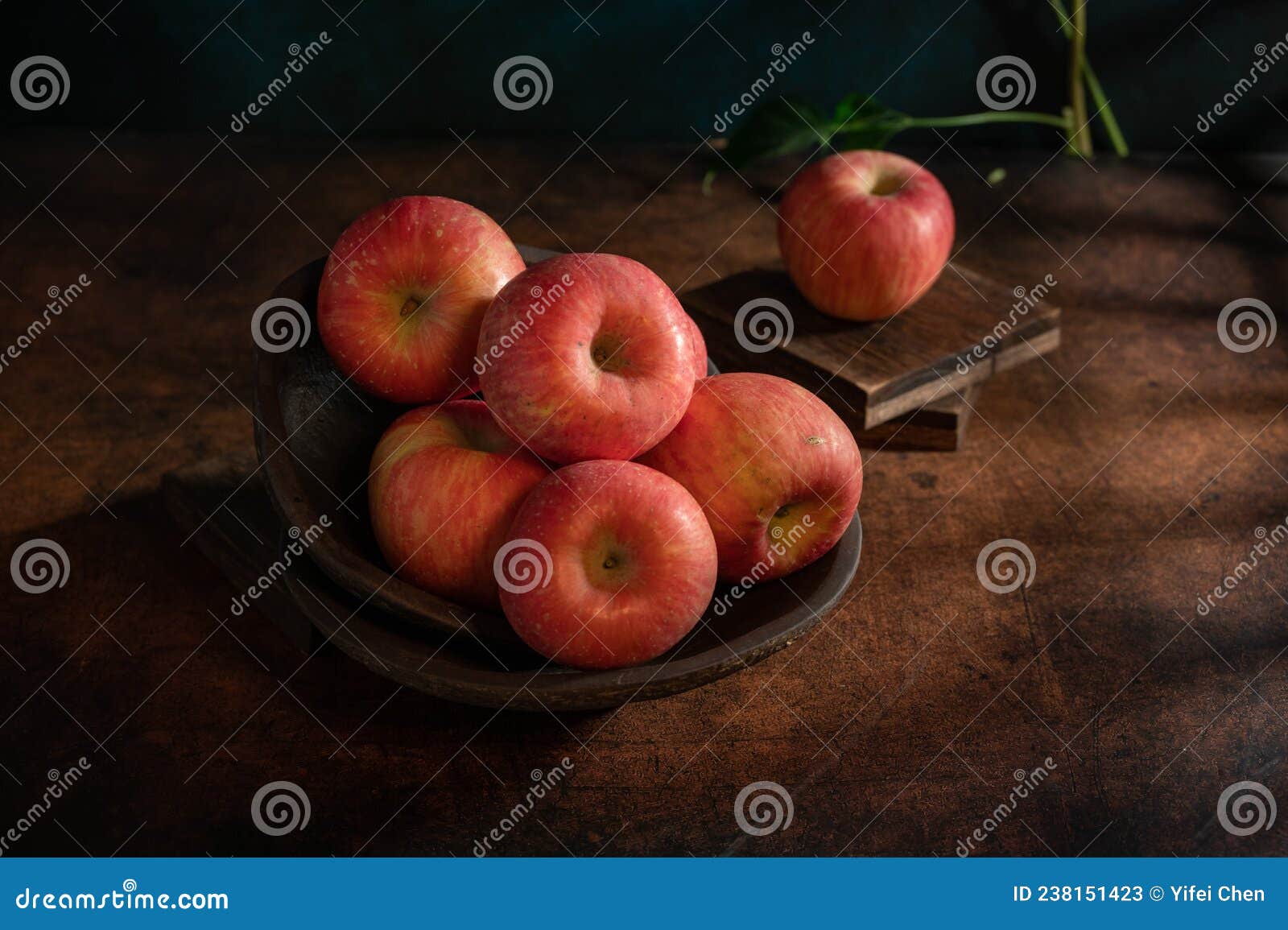 the apples on the plate look like oil paintings under the dim light on the wood grain table