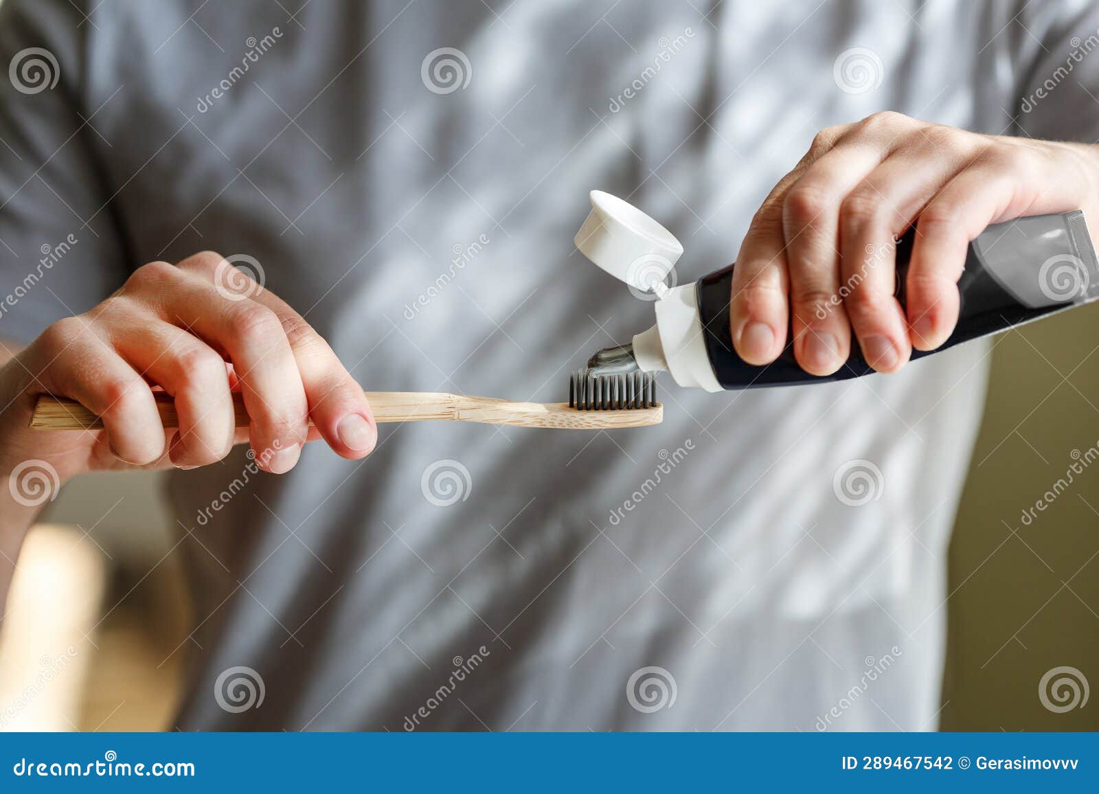 Applying Toothpaste on a Bamboo Tooth Brush. Hands Squeezing Tube with