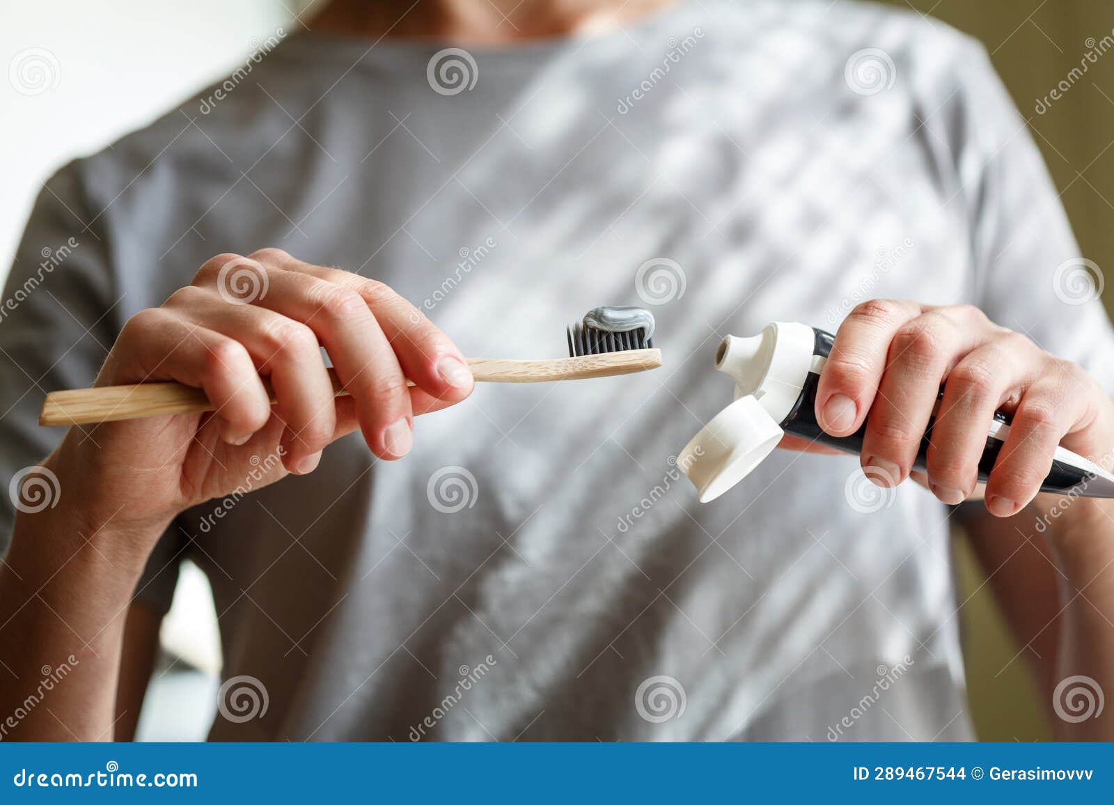 Applying Toothpaste on a Bamboo Tooth Brush. Hands Squeezing Tube with