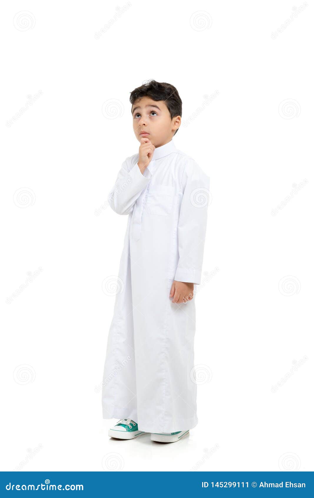 arab boy with a confused look and his hand on chin, looking up, wearing white traditional saudi thobe and sneakers, raising his