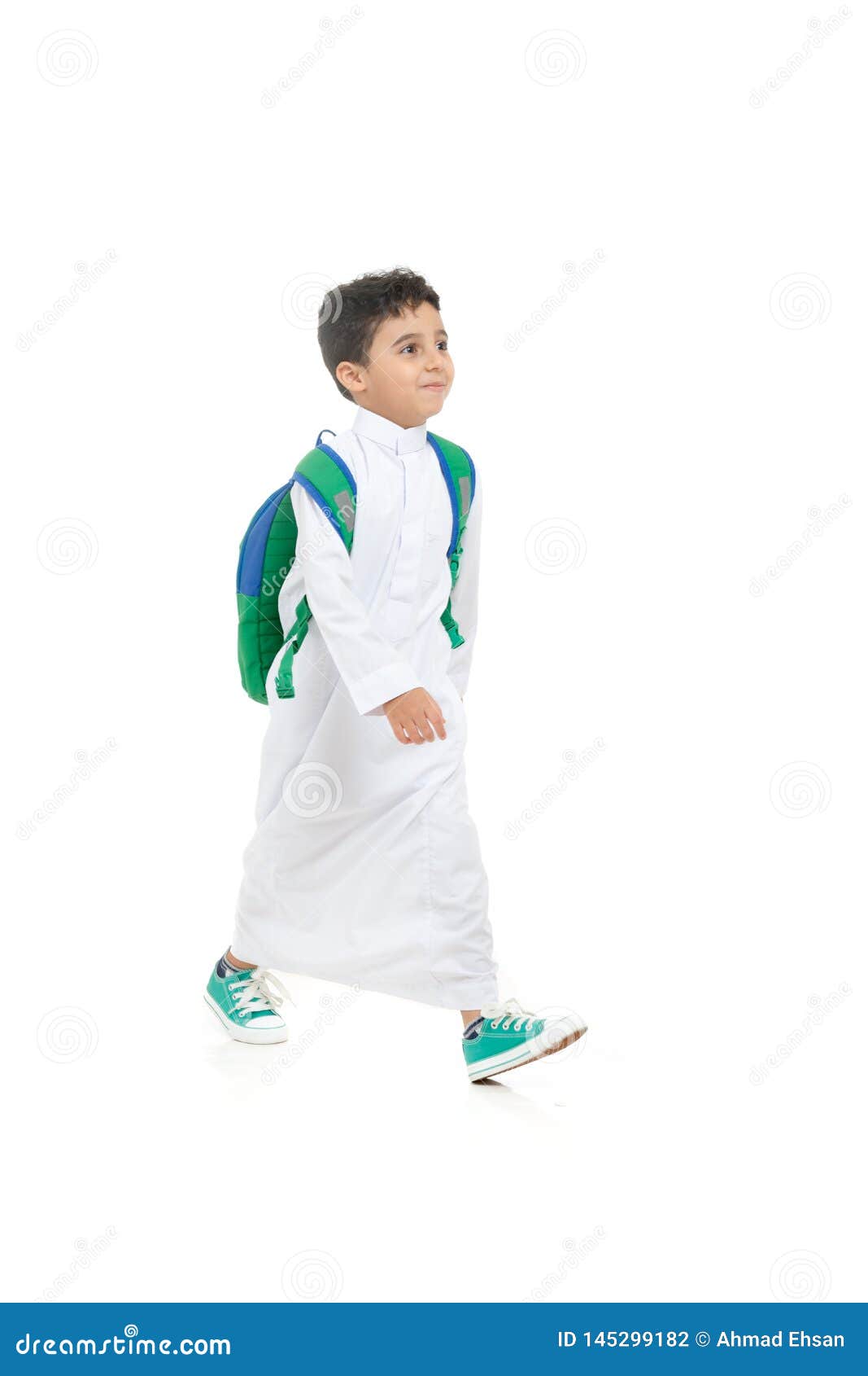 arab school boy smiling and walking, wearing white traditional saudi thobe, back pack and sneakers, raising his hands on white