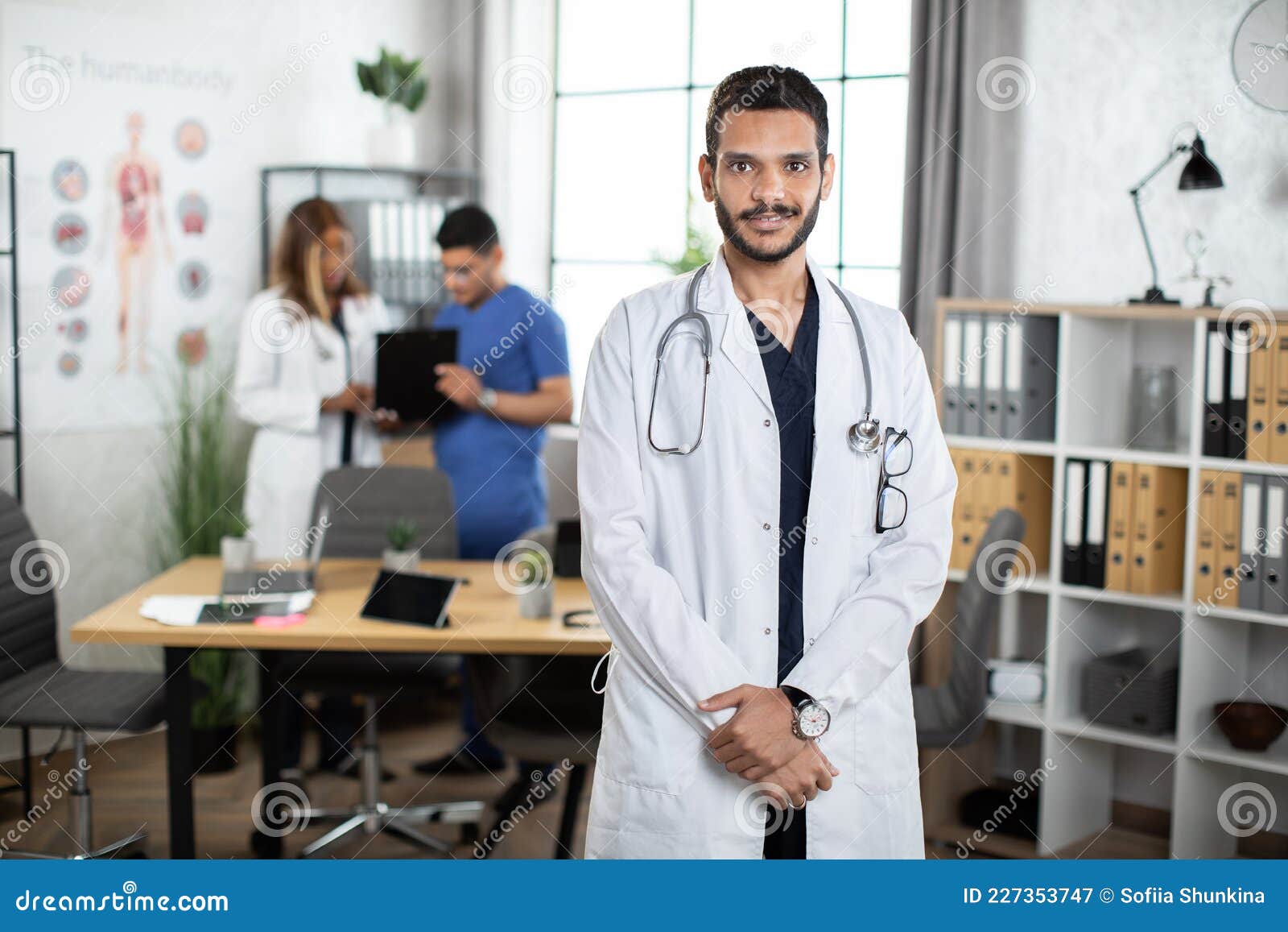 Arabic Male Doctor in Scrubs and White Coat, Posing at Camera Indoors