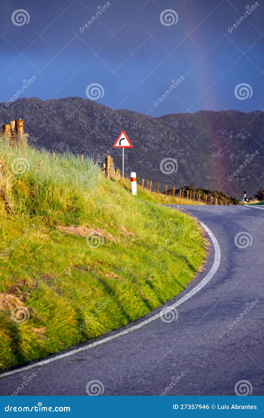 Arc-en-ciel ensuite qui courbent. Montagnes dans les montagnes écossaises (près de Mallaig) sous la lumière de coucher du soleil, une courbe sur la route sur le plan ; une route signent dedans la position de compromis et un arc-en-ciel et des montagnes dans le dos.