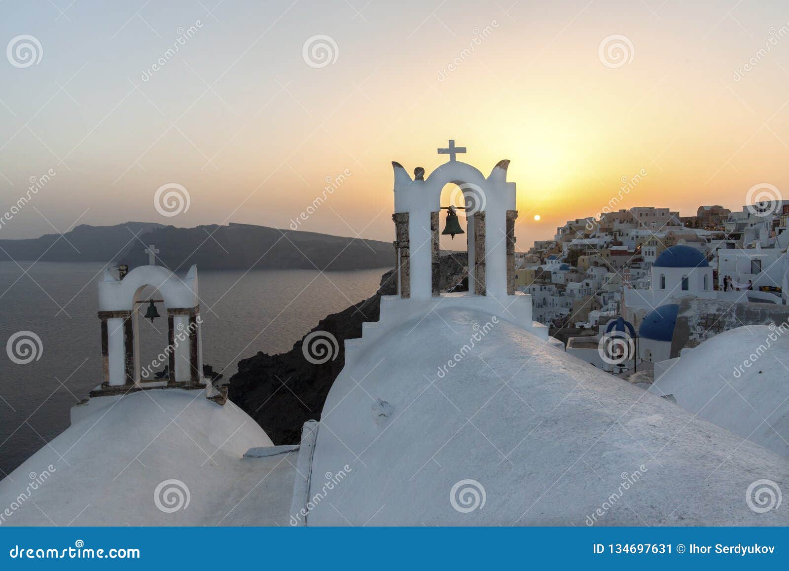 arch with a bell, white houses and church with blue domes in oia or ia at golden sunset, island santorini, greece. - immagine