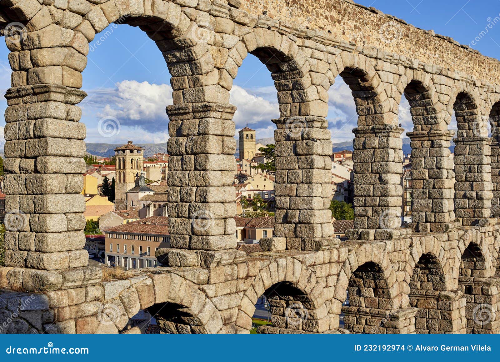 arch detail of the aqueduct of segovia, with the tower bell of the saint justo y pastor church in the background. view from