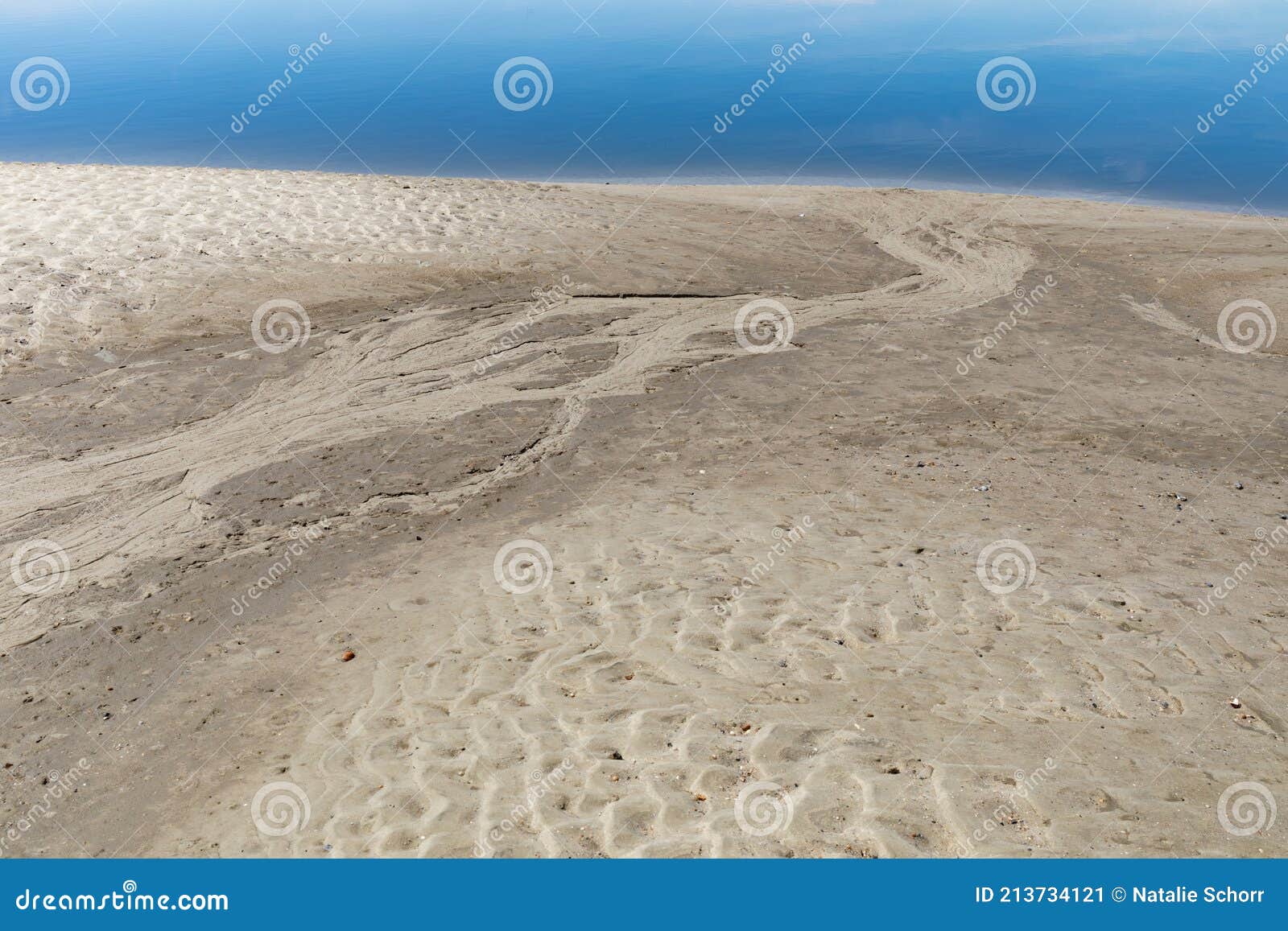 area of beach erosion from a previous flow of fresh water across a large swath of sand, blue waters beyond
