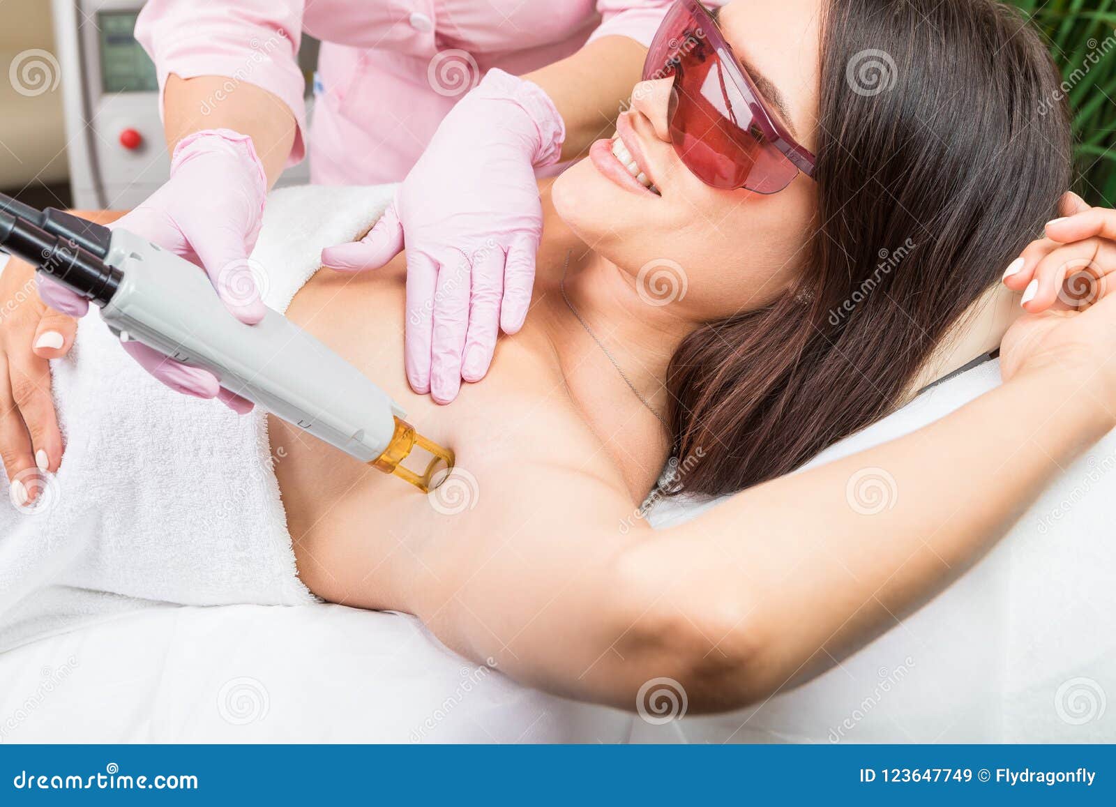 armpit laser hair removal. beautiful smiling woman client in red glasses having procedure.
