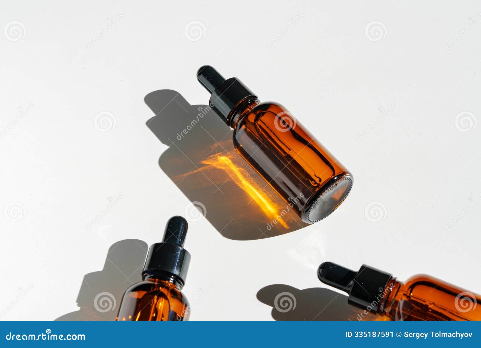 arranged amber glass bottles with droppers on white surface accentuated by shadows in bright light
