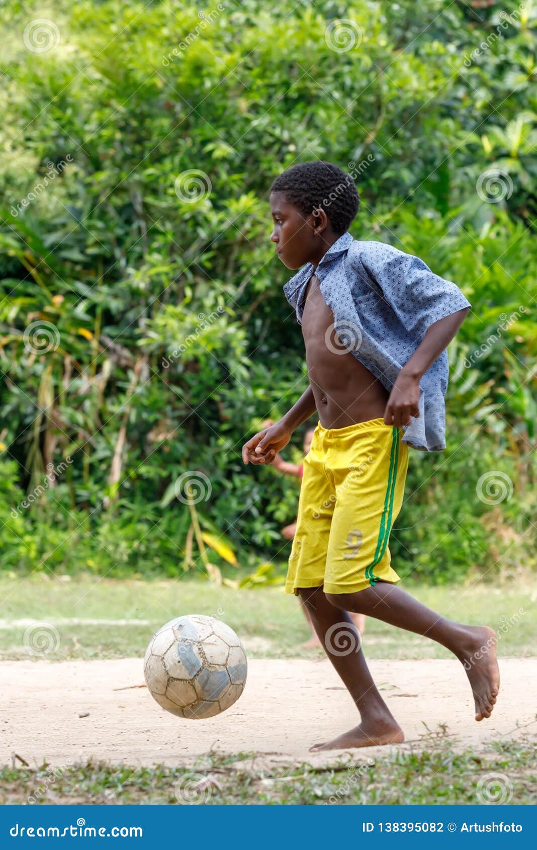 Garoto Joga Bola De Futebol Na Praia Arenosa. Pés Descalços De