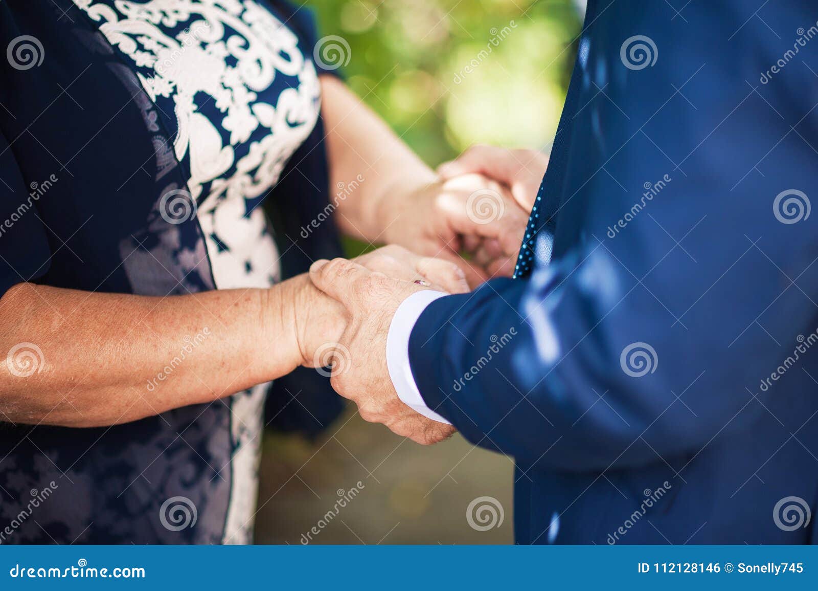 Пожилые держатся за руки. Мама жмет руку сыну. Рука пожилой матери держит руку сына. Мама держит сына за руку на свадьбе. Итальянская свадьба мама держит сына за руку.