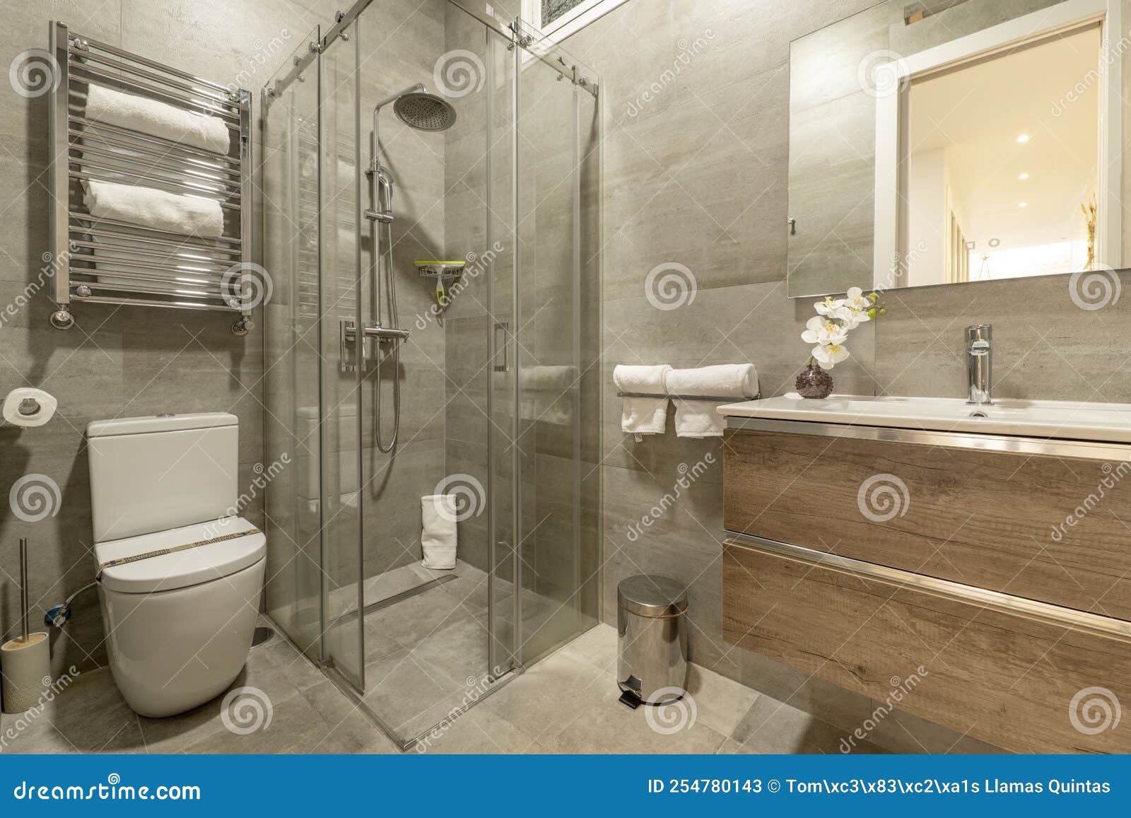 bathroom with oak wood chest of drawers with imitation marble tiles, frameless mirror on the wall and glass shower cabin
