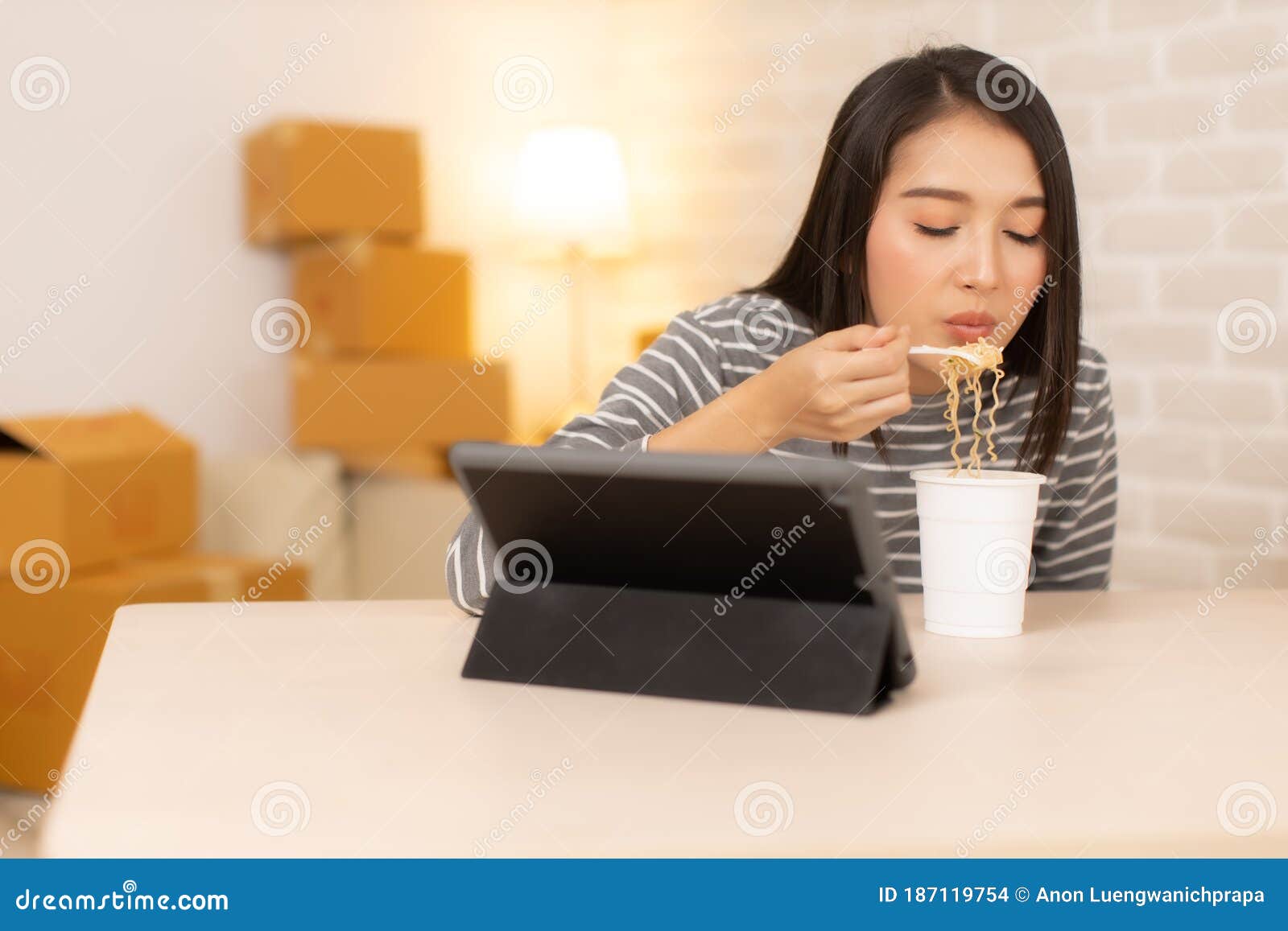asia freelance  business woman eating instant noodles while working on laptop in living room at home office at night. young asian