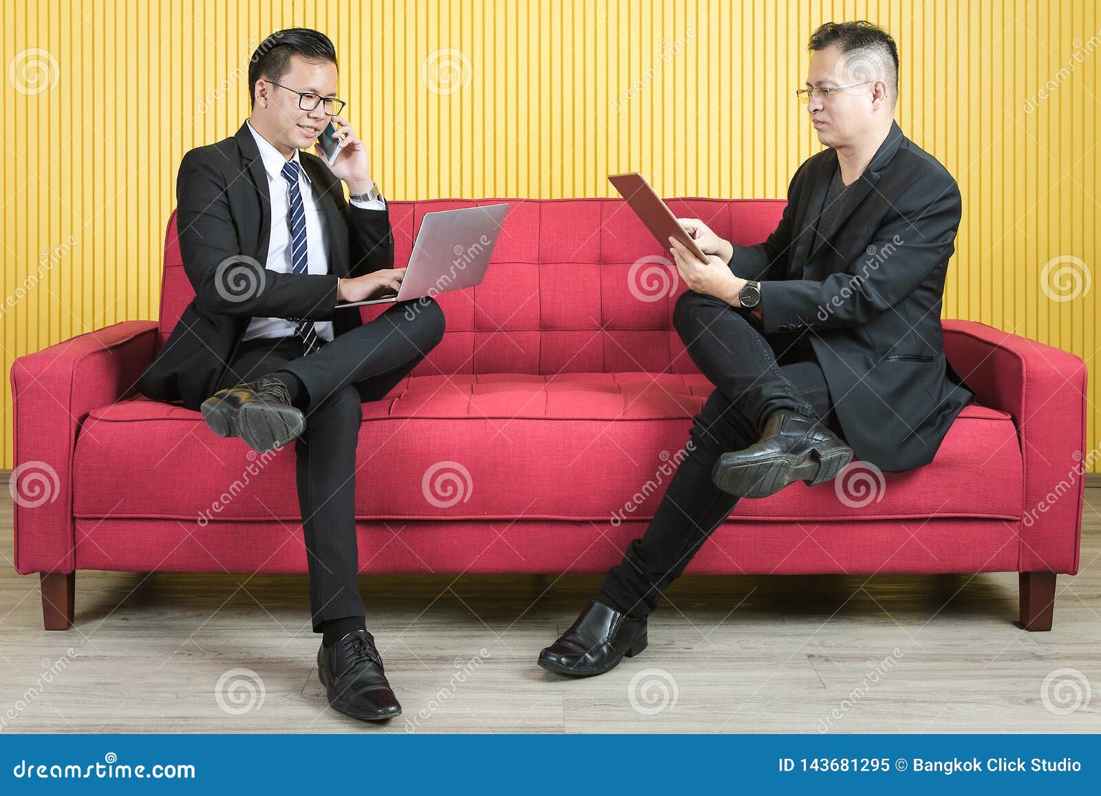 Asian businessman at office. Young and middle aged Asian businessmen wearing eyeglasses in dark suit, both busily checking data from tablet and notebook, working on new project in modern living room background