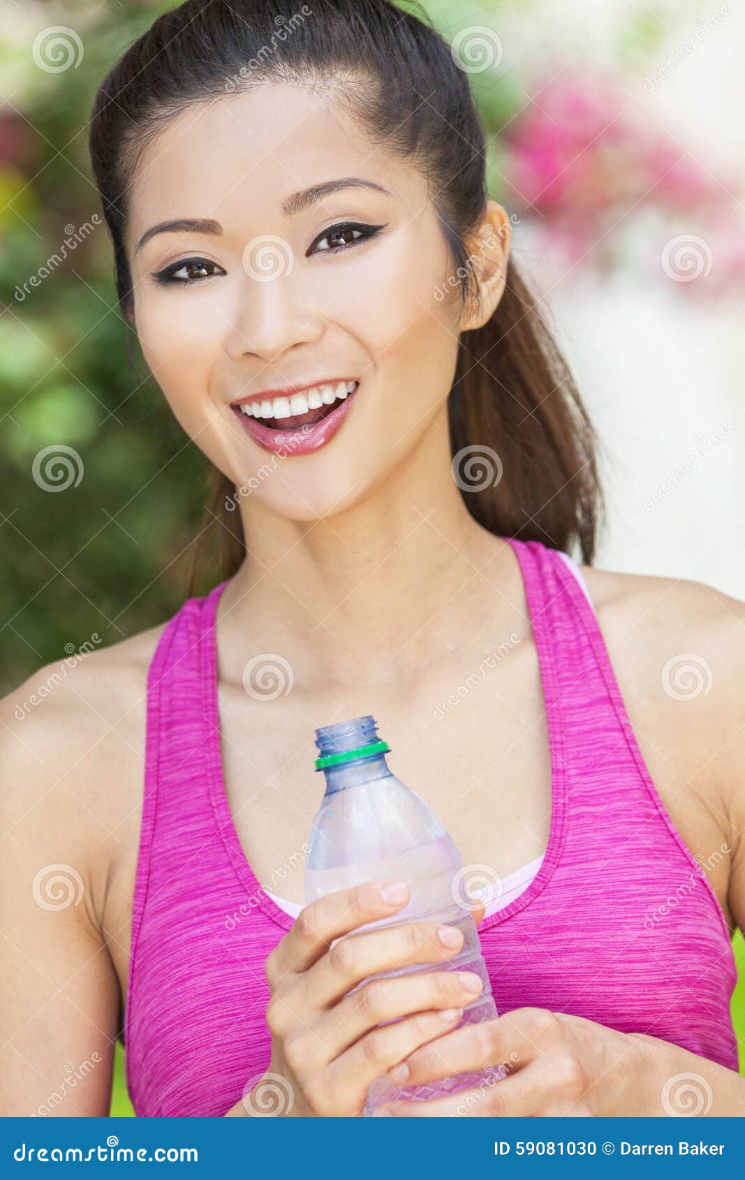 Asian Chinese Woman Exercising Drinking Bottle of Water. Beautiful Chinese Asian girl or young woman smiling, exercising and drinking a bottle of water outside