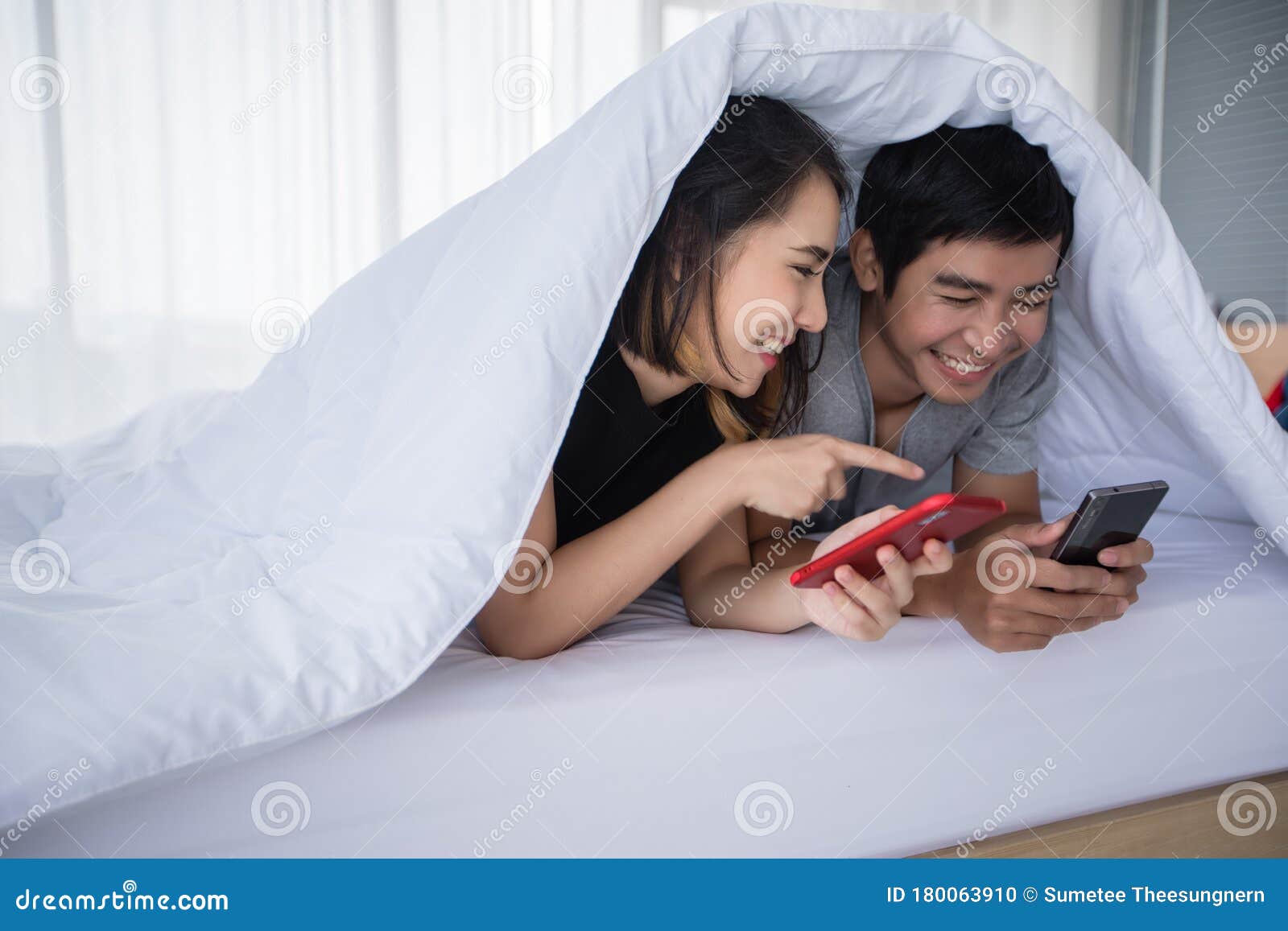 Asian Couple Lovers Lying On Their Play Mobile Phones On Bed At Home