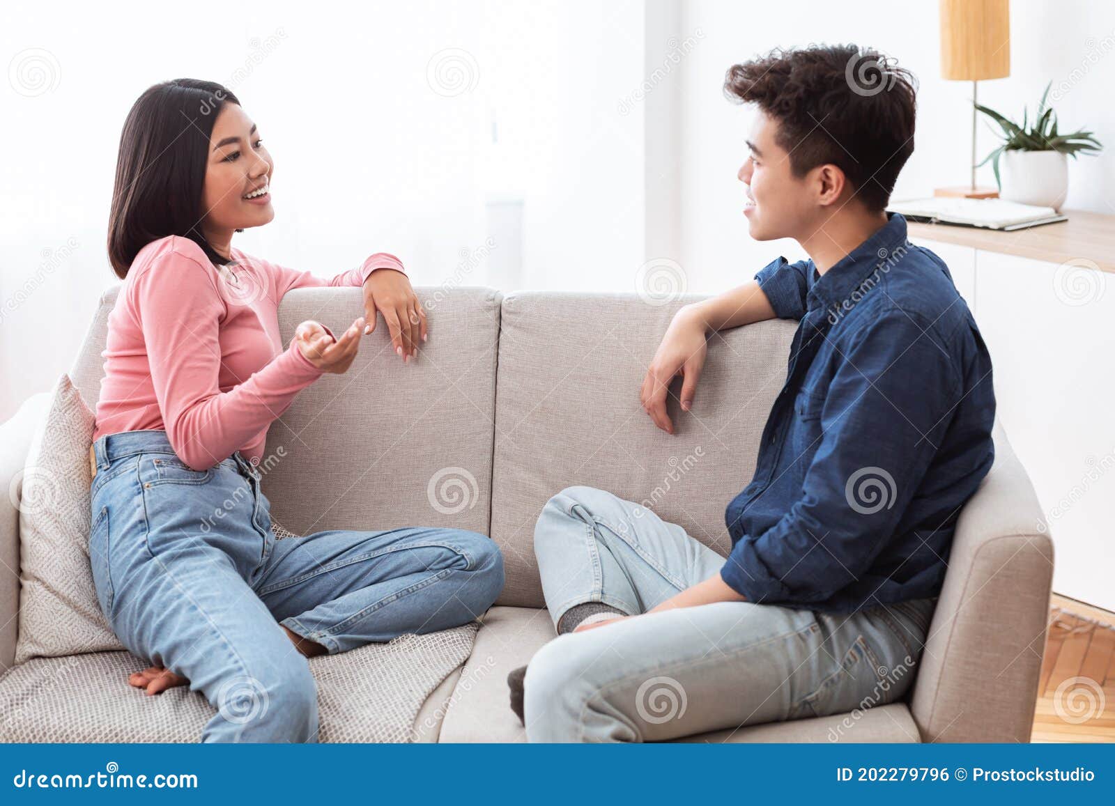 Asian Couple Talking Enjoying Conversation Sitting On Couch At Home