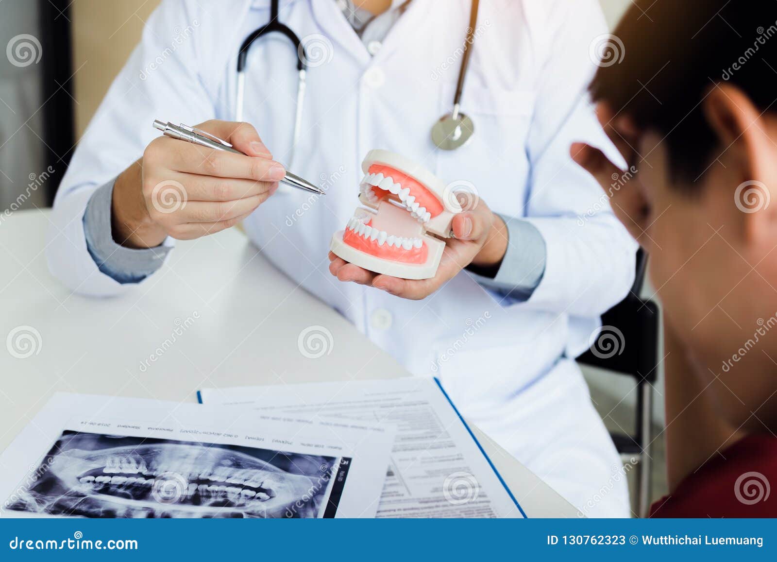 asian dentist holding pen pointing to the dentures and is describing the problem of teeth.
