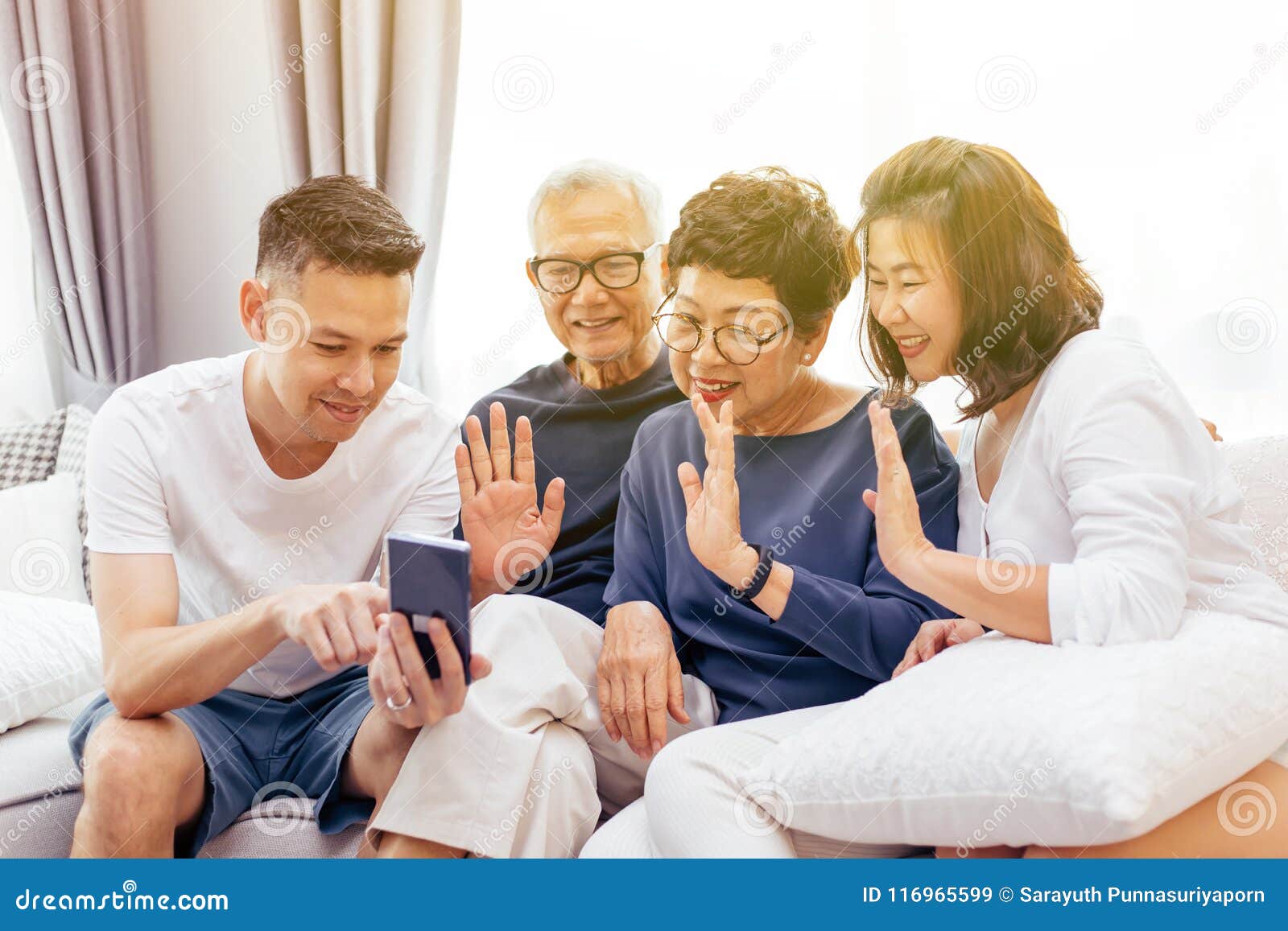 asian family with adult children and senior parents making a video call and waving at the caller at home.