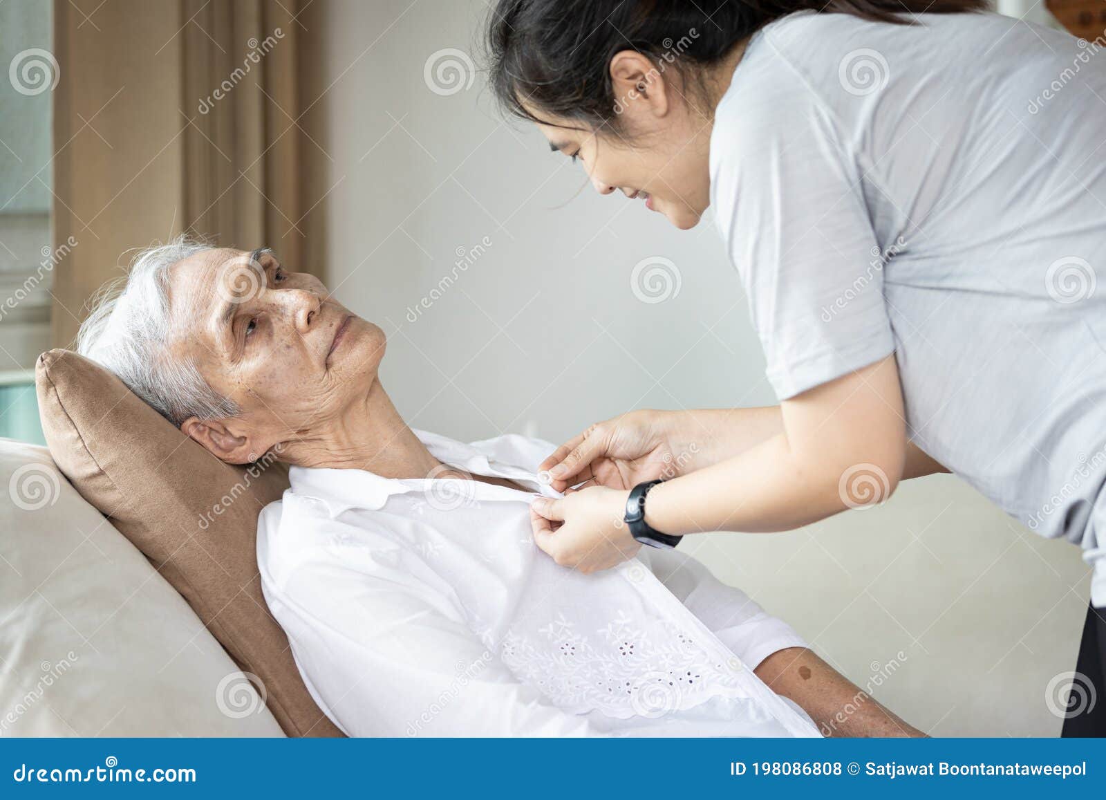 asian female caregiver taking care of helping elderly patient get dressed,button on the shirt or changing clothes for a paralyzed