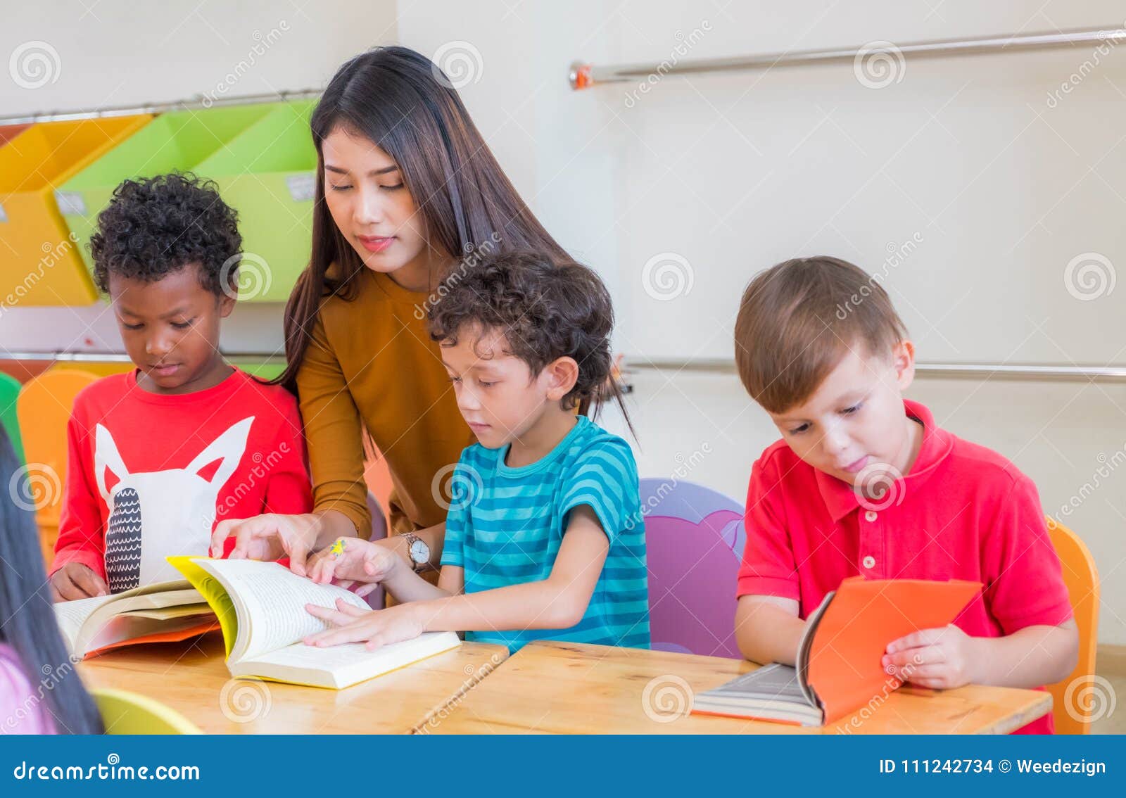 asian female teacher teaching diversity kids reading book in classroom,kindergarten pre school concept.