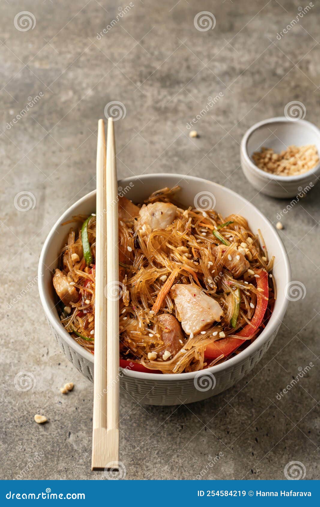 asian funchose salad with chicken and vegetables in bowl with wooden chopsticks on textured green background with text