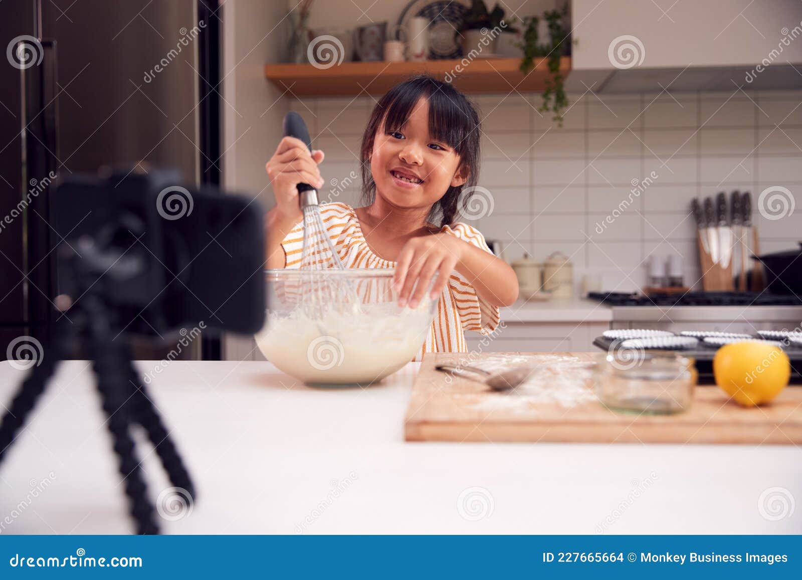asian girl baking cupcakes in kitchen at home whilst on vlogging on mobile phone