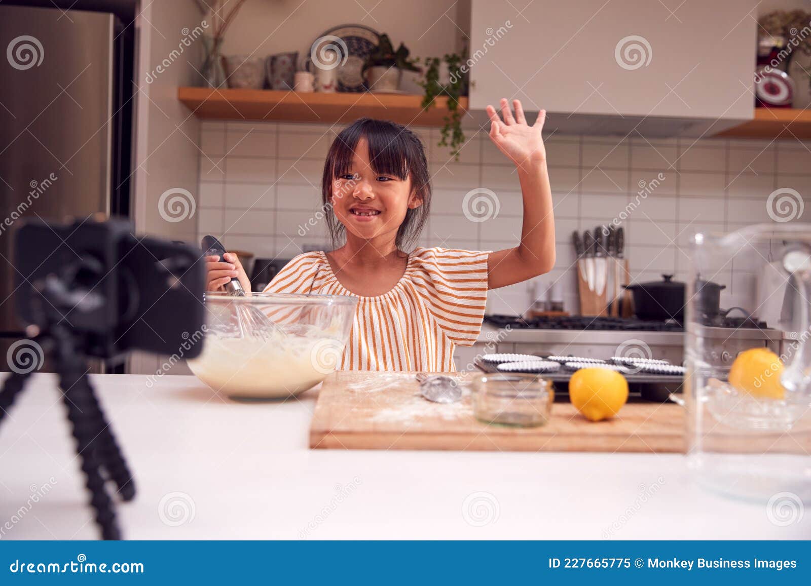 asian girl baking cupcakes in kitchen at home whilst on vlogging on mobile phone