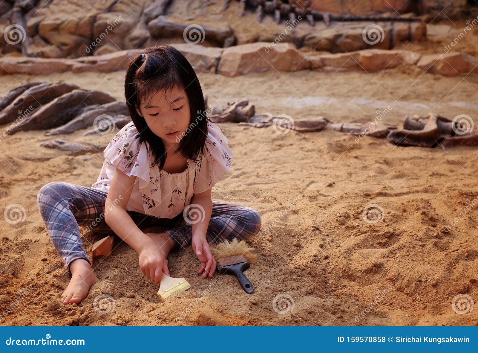 an asian girl playing in a sandbox with a modeled dinosaur fossil