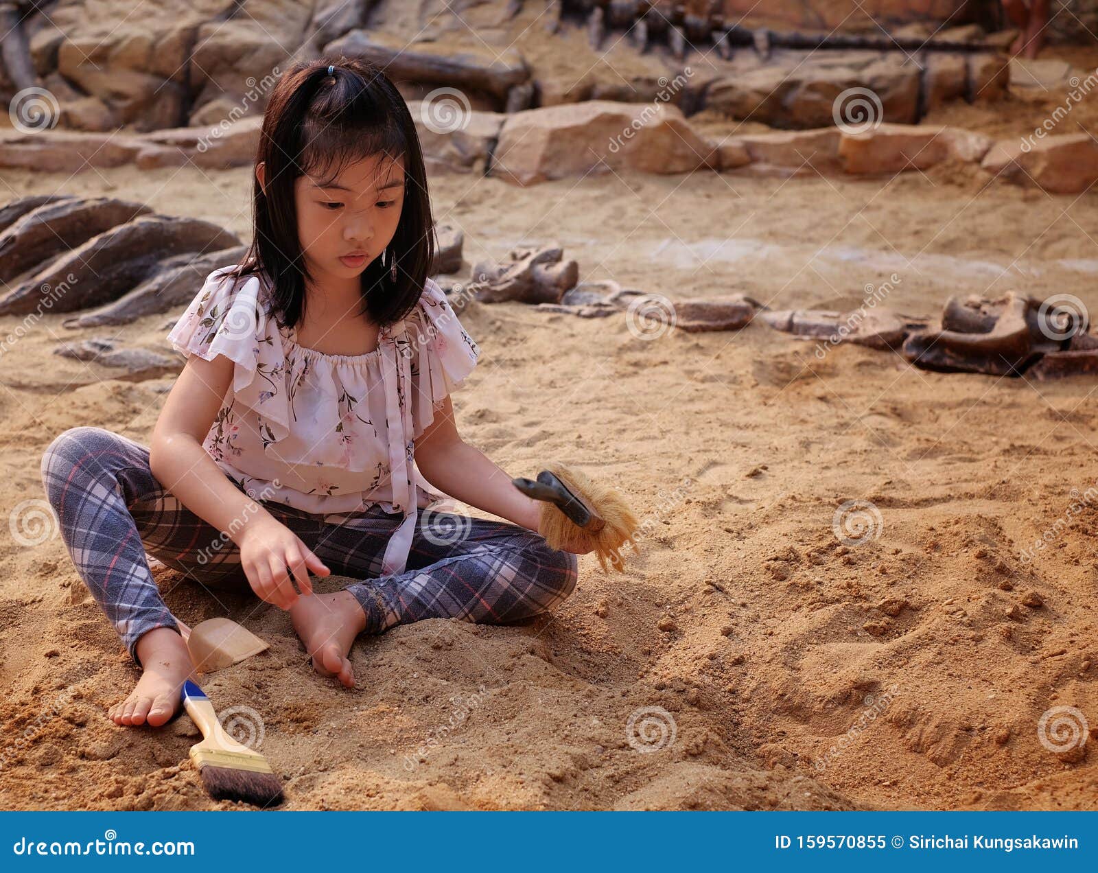 an asian girl playing in a sandbox with a modeled dinosaur fossil