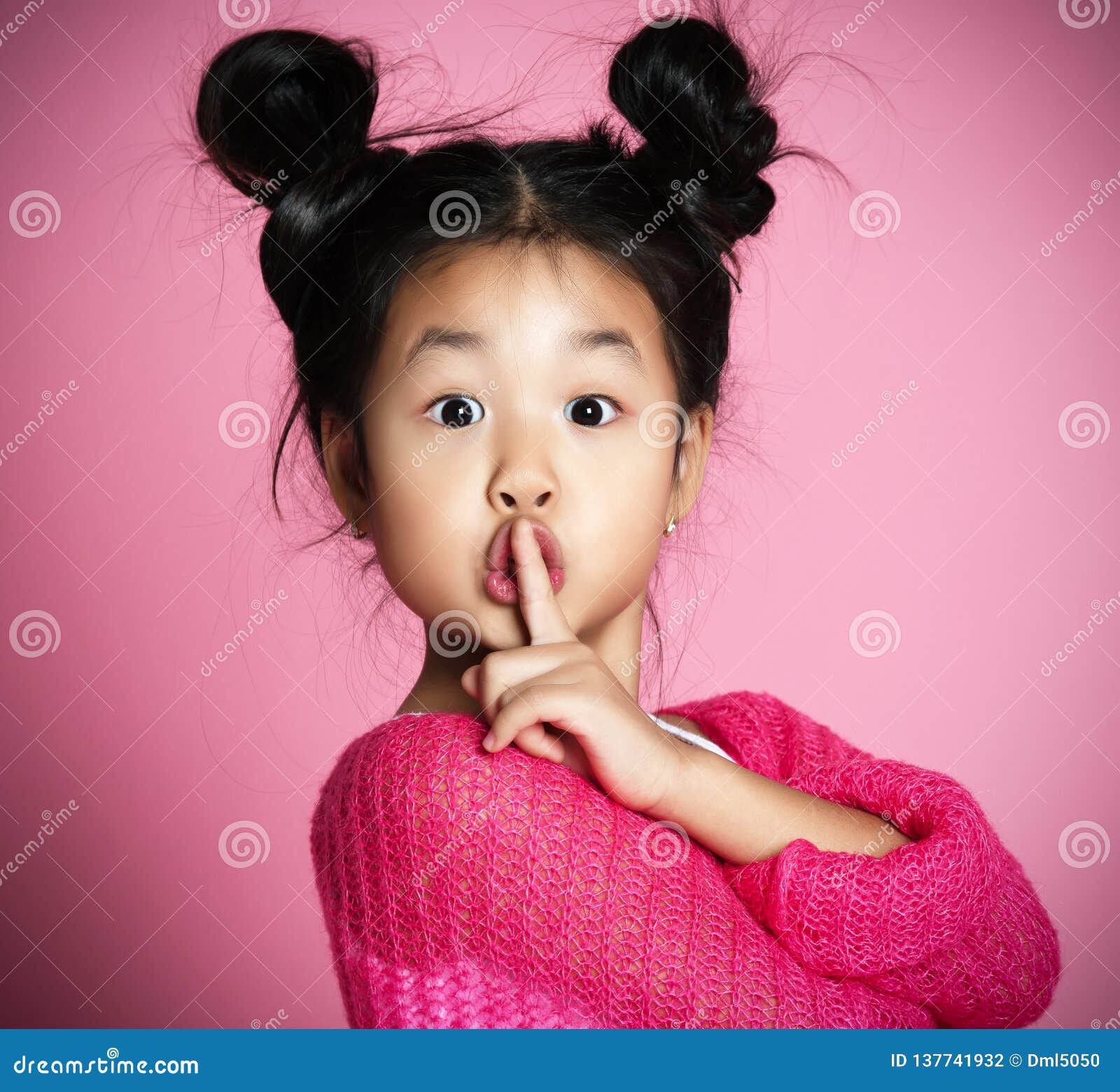 asian kid girl in pink sweater shows shh sign close up portrait