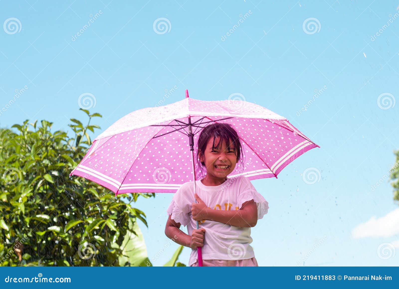 asian girl standing with an umbrella with joyfulness while it is raining and sunny during the day.