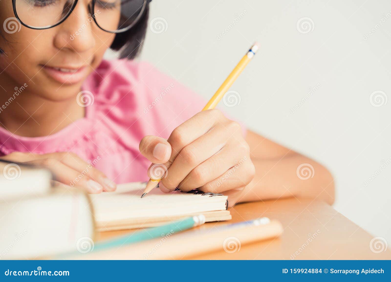 asian little girl wears glasses while sit writing on  desk at her home