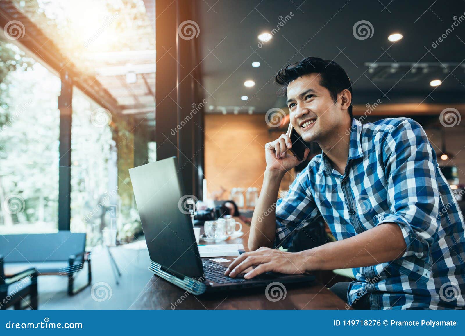 asian man freelance work on computer touch pad while talking on smart phone with a happy smile, young business man use laptop