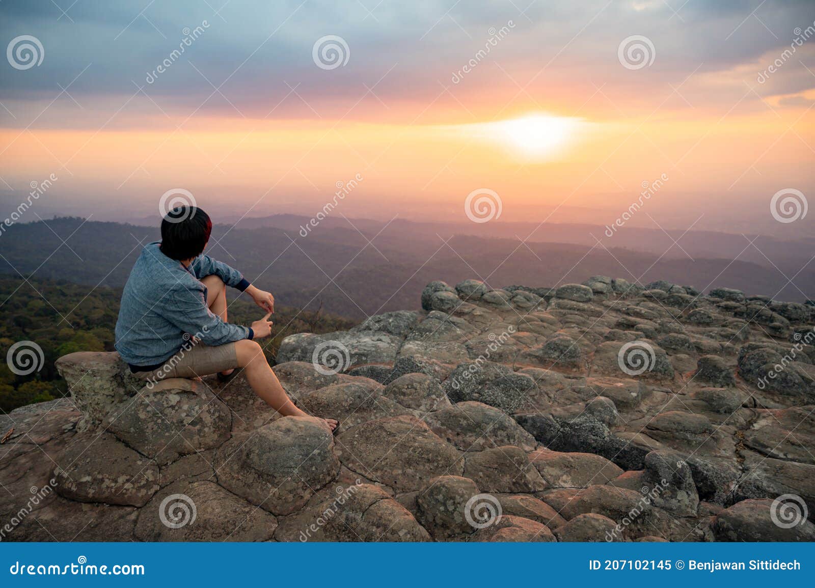 asian man sitting on nodule rock field enjoy looking sunset